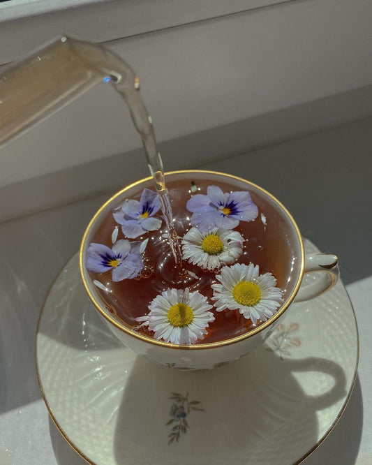 A warm glass of tea with flowers sits by a window, symbolizing a gentle start to the day.