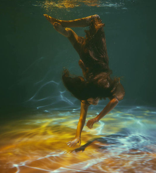 A woman submerged underwater, struggling to reach the surface, symbolizing the feeling of being trapped by limiting beliefs and expectations.